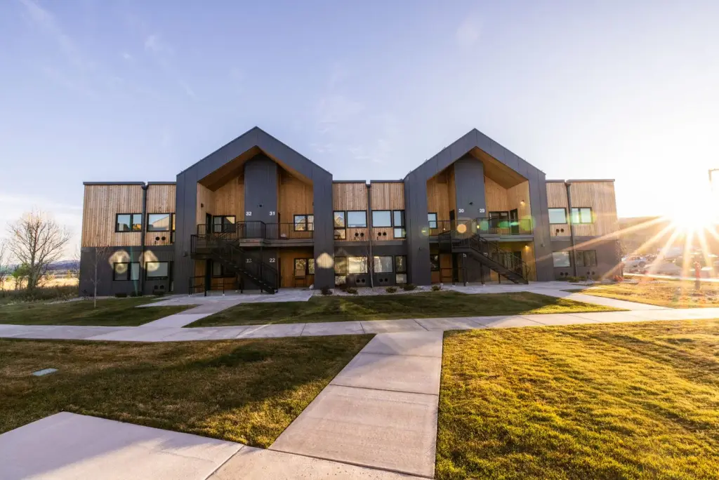 Street-side view of a two-story Teton Flats building with gabled entries, wood and dark metal siding, and lawn at sunset