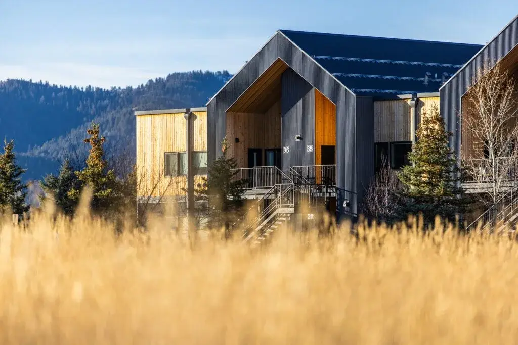 Wood and dark metal apartment buildings at Teton Flats in Victor, with golden grasses and wooded hills