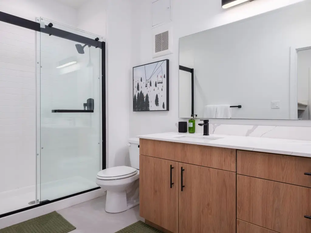 Staged one-bedroom model bathroom with glass shower, wood vanity, and quartz counter