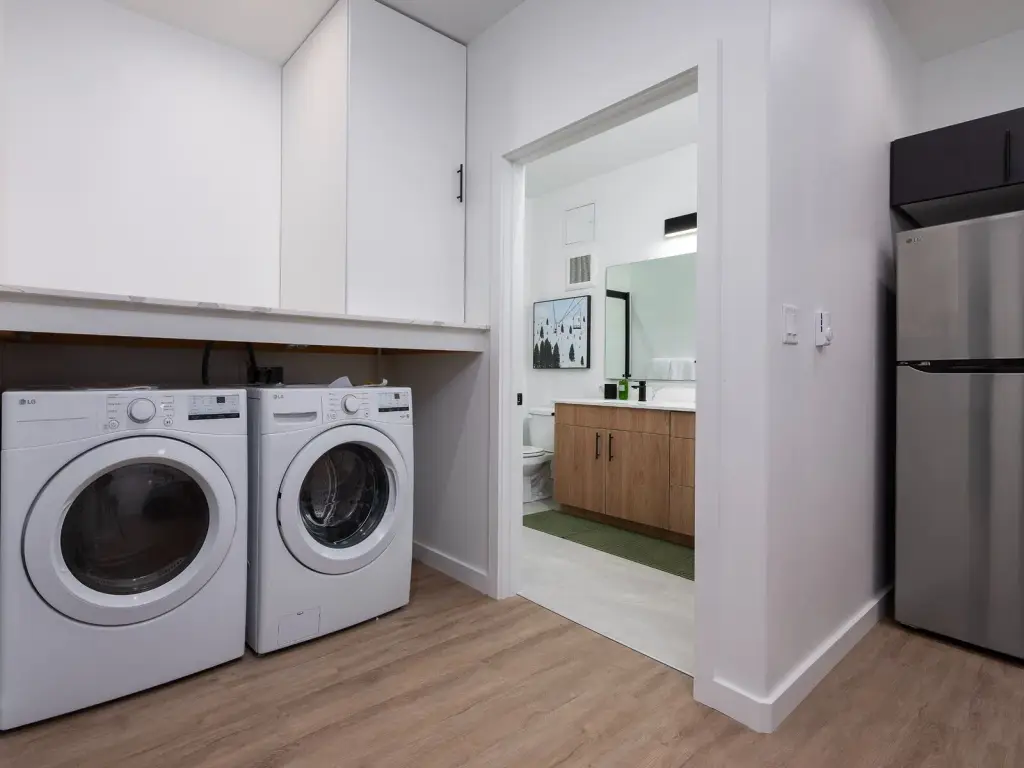 Staged one-bedroom model with in-unit washer and dryer beside the refrigerator, bathroom beyond