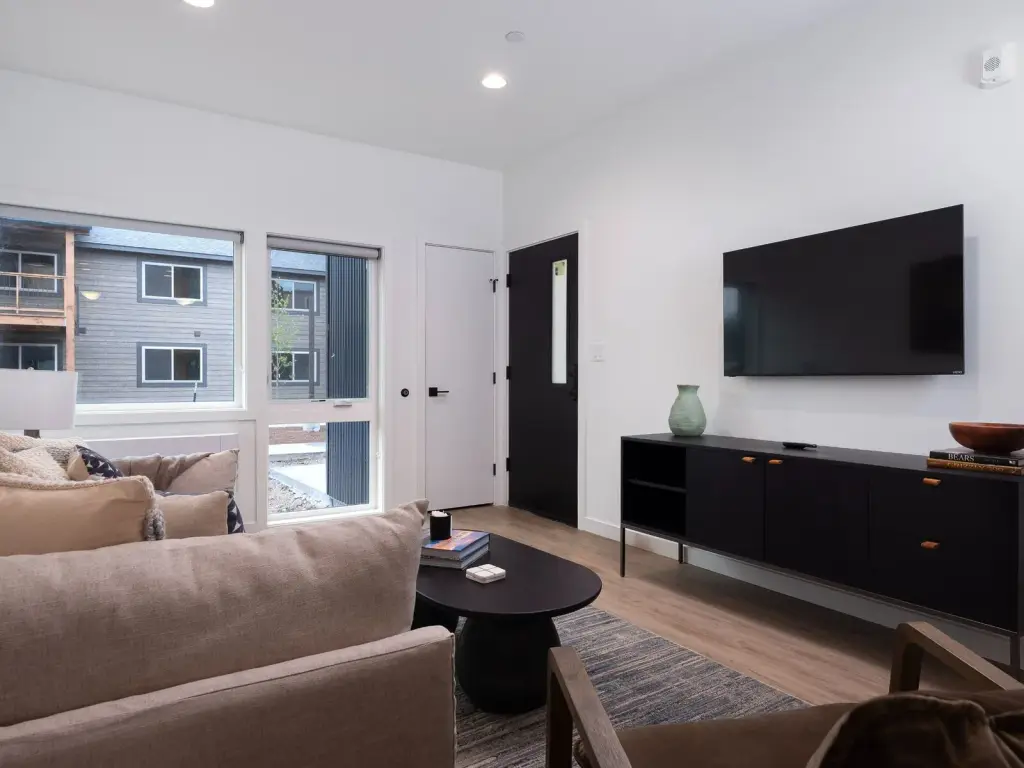 Staged one-bedroom model living room with a wall-mounted television and entry door